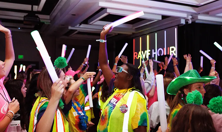 Students dressed in bright colors hold light-up sticks and dance during UA Miracle's dance marathon.