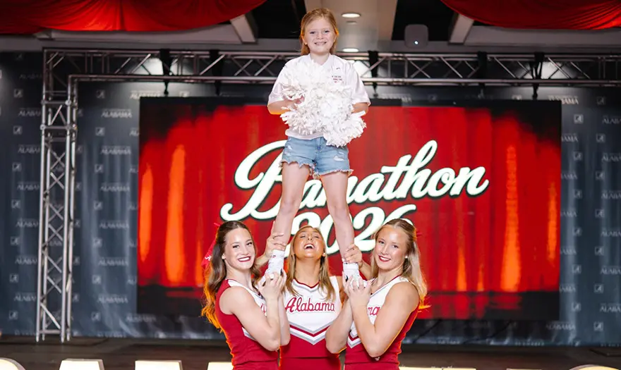 Members of the University of Alabama cheer team lift a child holding pompoms.