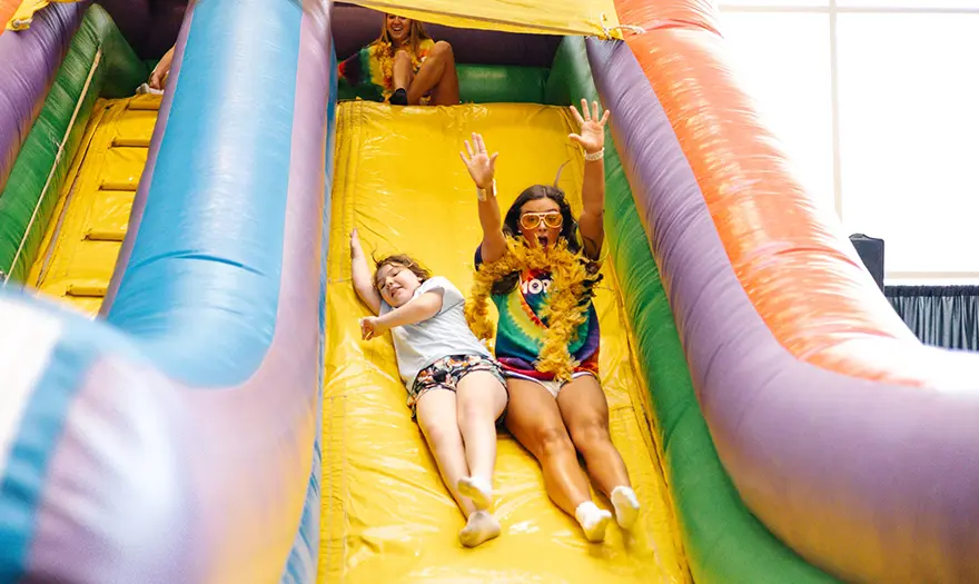 A child and a UA student slide down an inflatable slide. 